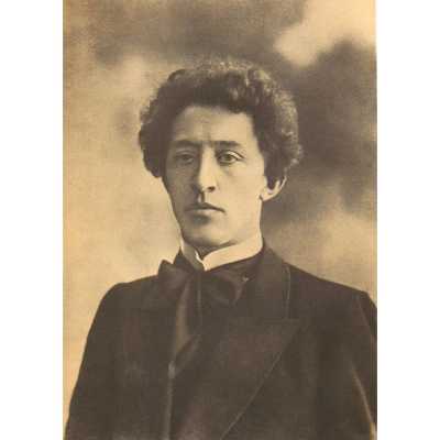 A sepia-toned photograph of a man with curly hair (locks) wearing a dark formal jacket (coat) and tie. His facial expression is neutral, and he is gazing slightly to the left of the viewer. The background is blurred with no distinguishable features."