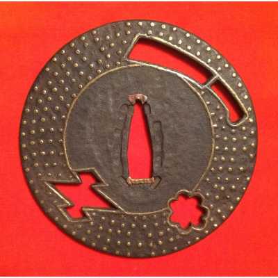 A metal tsuba (sword guard) featuring a geometric cut-out pattern (design), with raised dots (studs) and a single flower motif (blossoms). The guard includes two notches (slots) for blade attachment."
