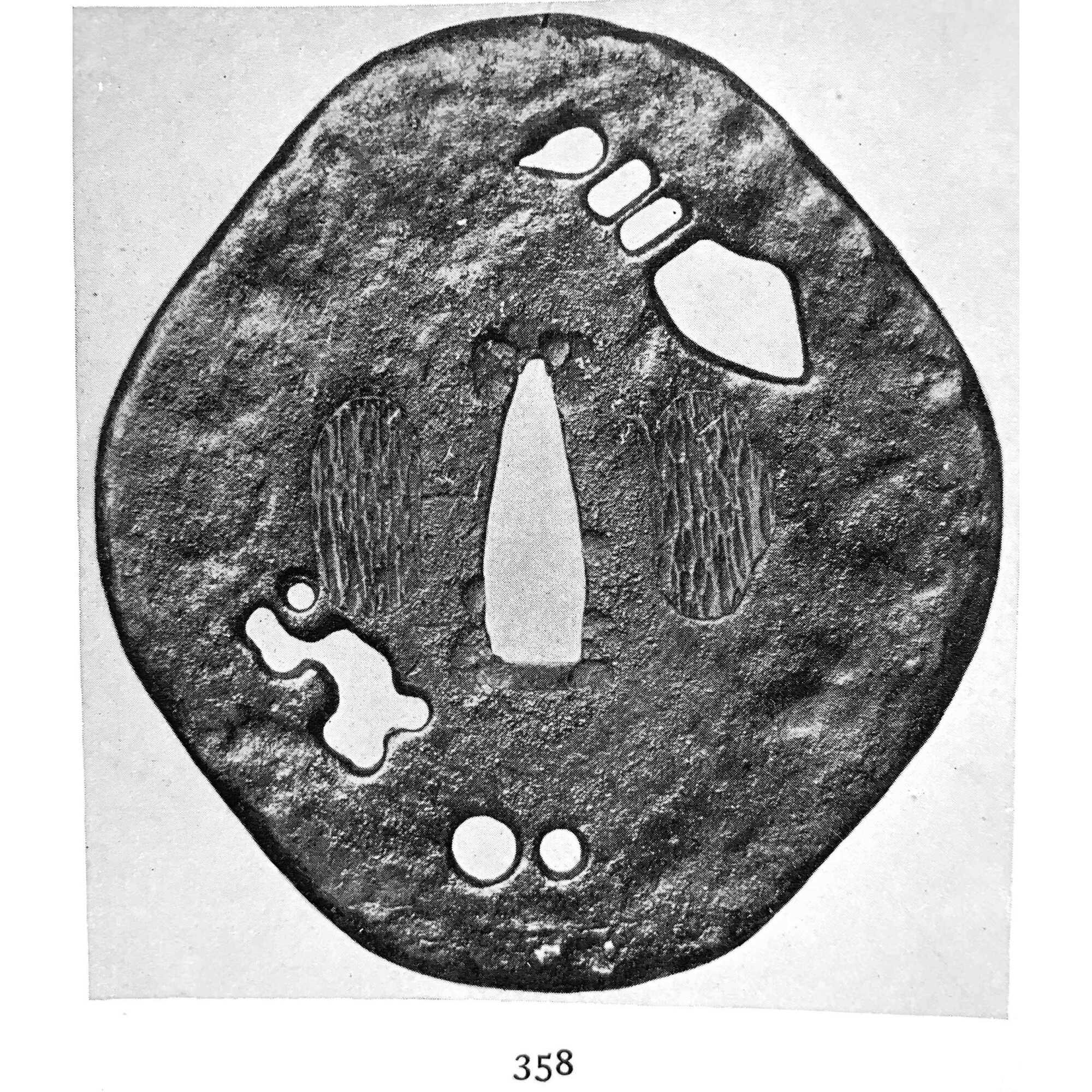A metal tsuba (sword guard) with several cut-out (pierced) shapes, including an abstract pattern (design) and circular forms. The guard features textured surfaces (areas) suggesting either wear or deliberate patterning."